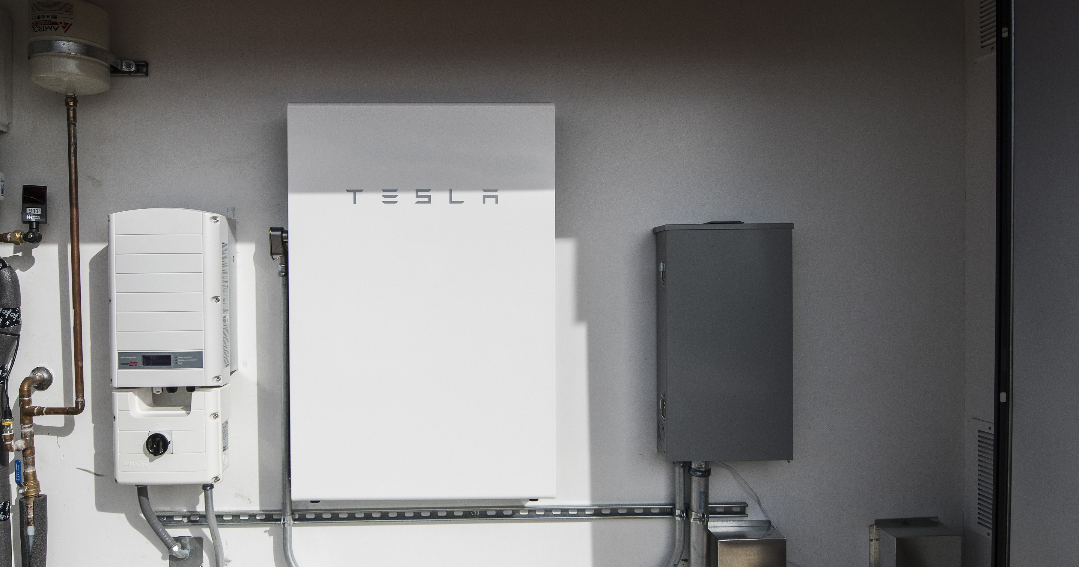 A wall-mounted home battery and solar inverter installed in a residential utility space.