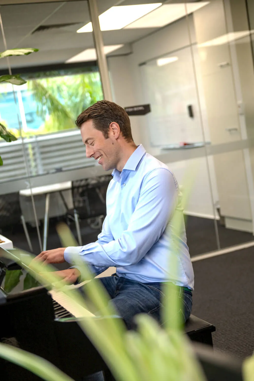 A man playing the piano with a plant in the foreground