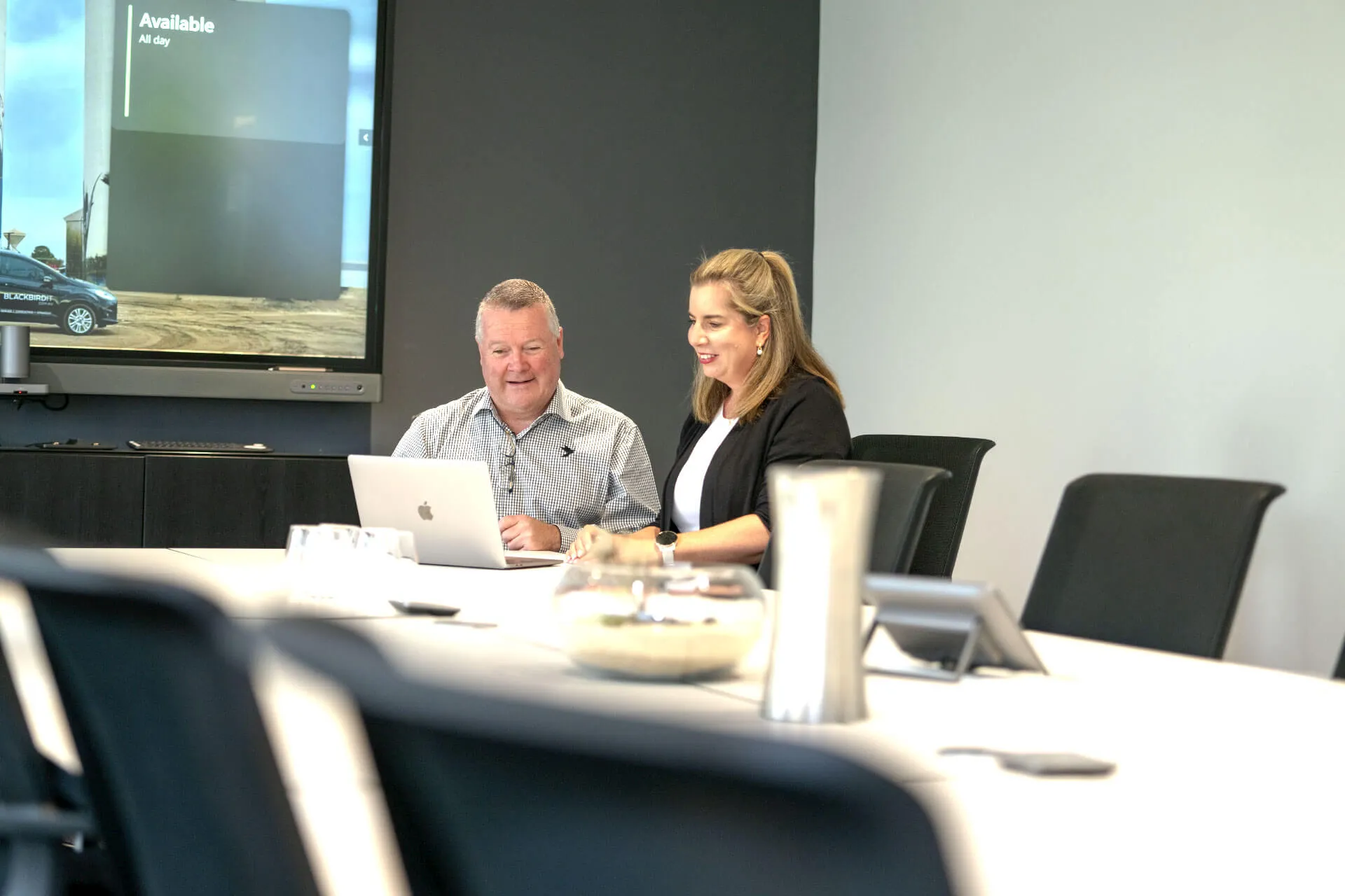 a man and a woman sitting at a table in front of a laptop