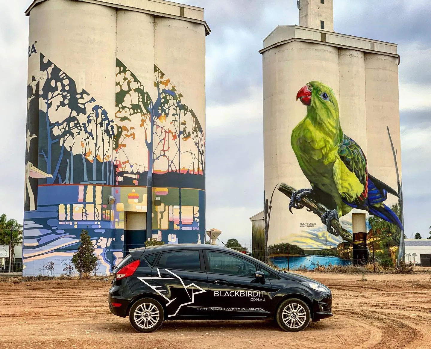 a black car parked in front of two large silos