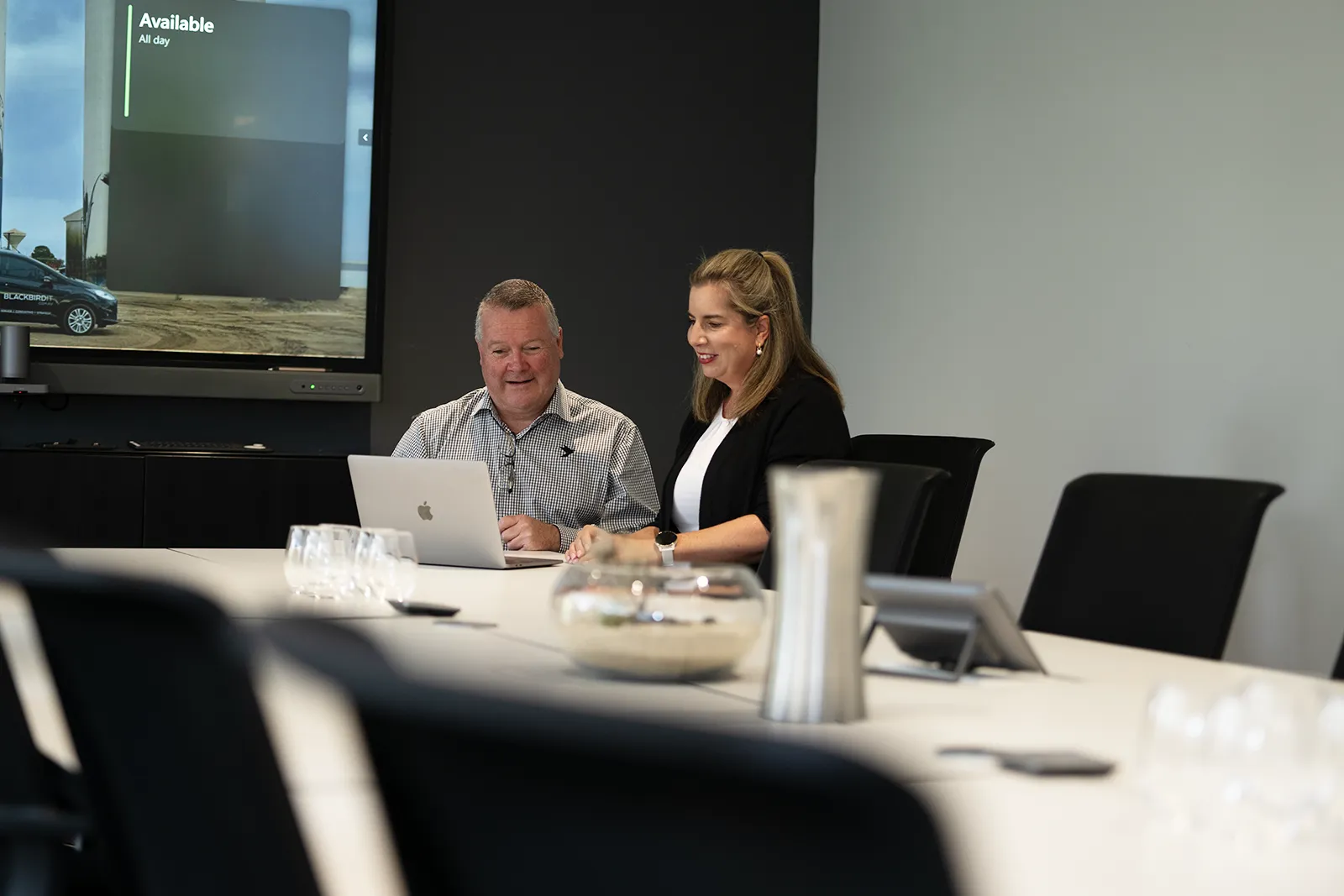 a man and a woman sitting at a table in front of a laptop