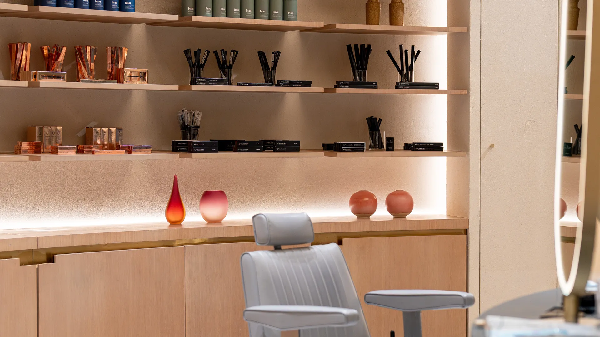 Modern salon interior with neatly arranged beauty products on wooden shelves and a gray salon chair in front.