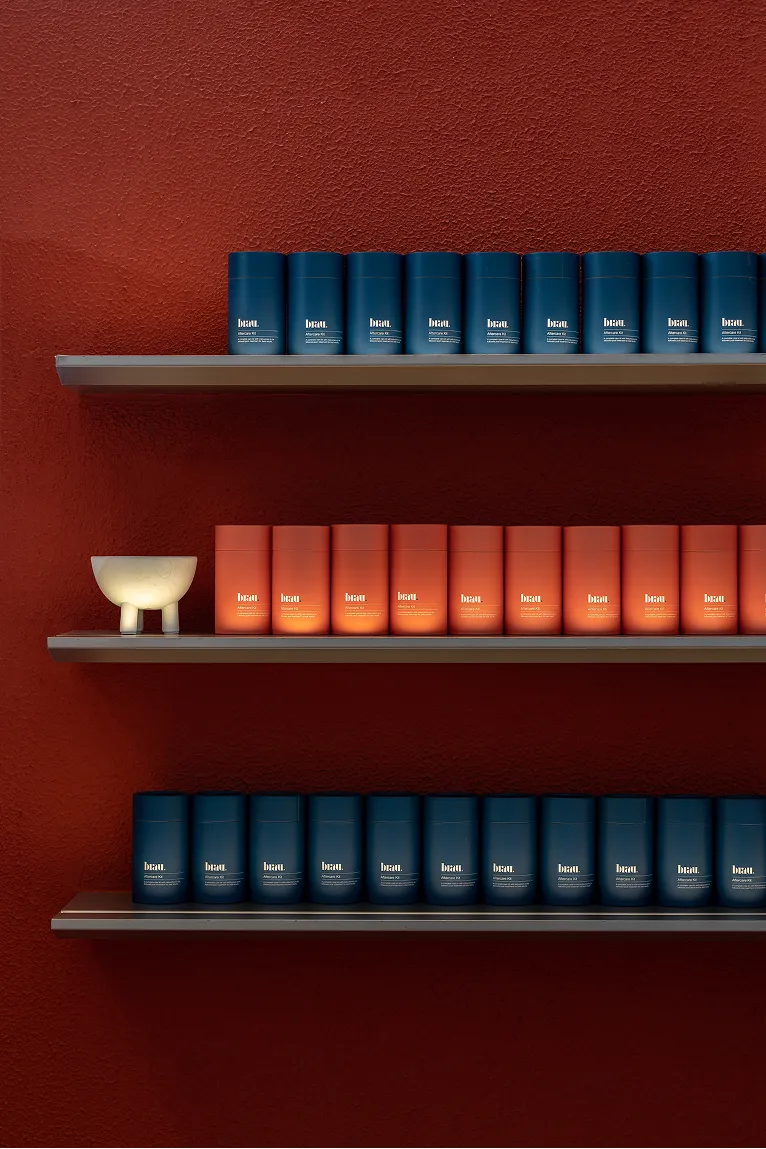 Three shelves against a textured reddish-brown wall displaying blue and orange cylindrical product containers, with a small white bowl on the middle shelf.