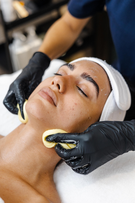 أخصائية تجميل تمسح البشرة بعناية لتنظيفها بعد انتهاء العلاج