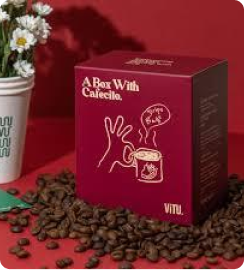 Red box of VITU coffee surrounded by coffee beans with a drawing of a steaming coffee cup and flowers in a white vase in the background.