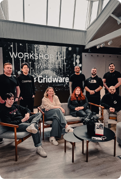 Group of eight people posing inside a modern workspace with large windows and a sign reading 'Workshop Gridware.'