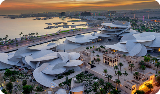 Aerial view of the National Museum of Qatar with its distinctive interlocking disc architecture near the coast at sunset.