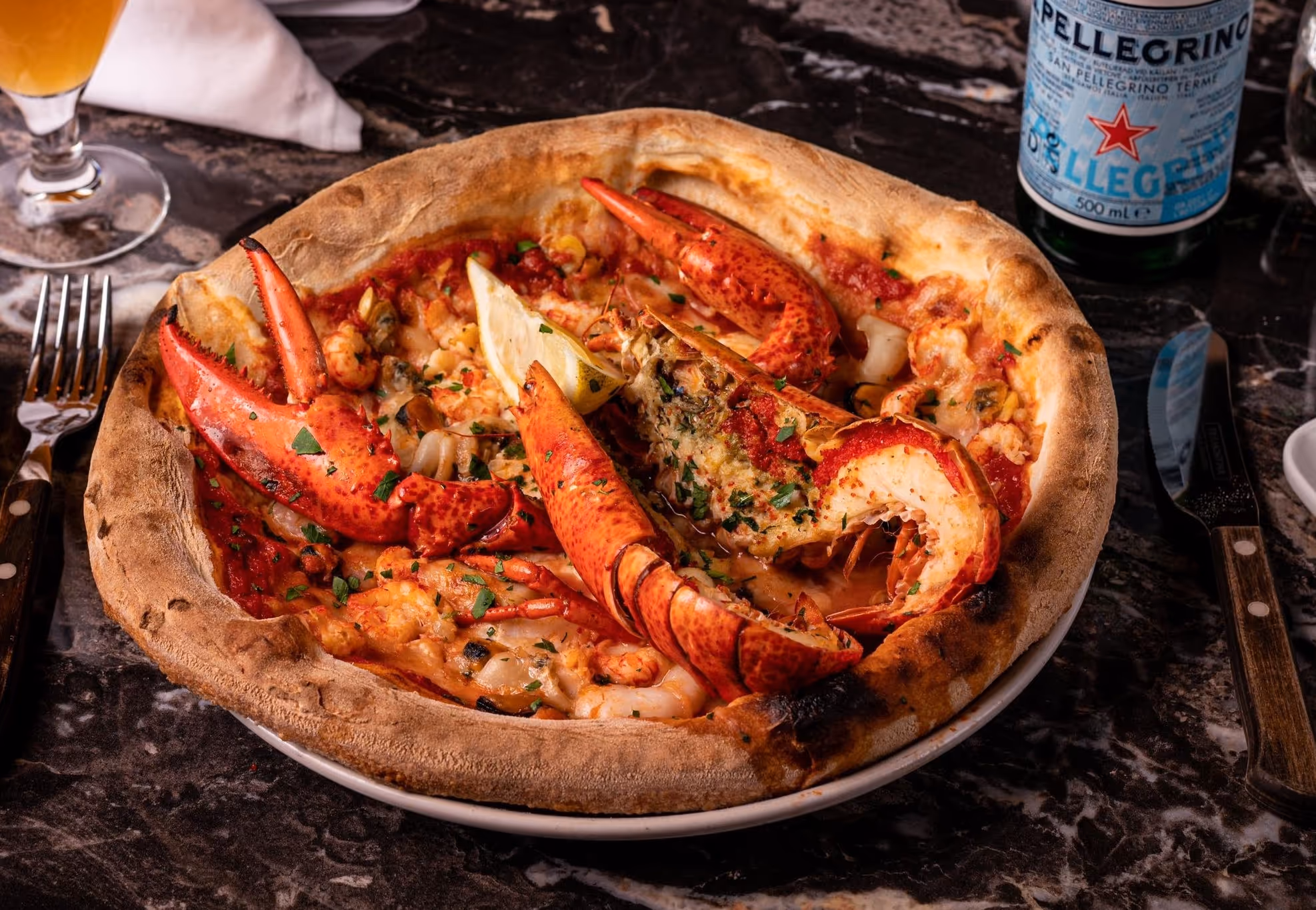 Gourmet hummerpizza servert på Riviera Restaurant i Oslo, toppet med fersk sjømat, urter og sitron.
