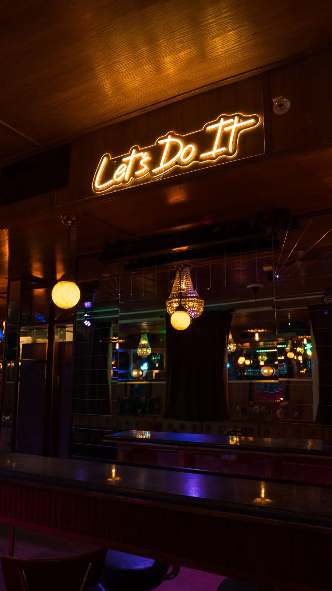 Neonskilt med teksten Let's Do It i selskapslokalet til Riviera Restaurant i Oslo, omgitt av varme lys og speil.