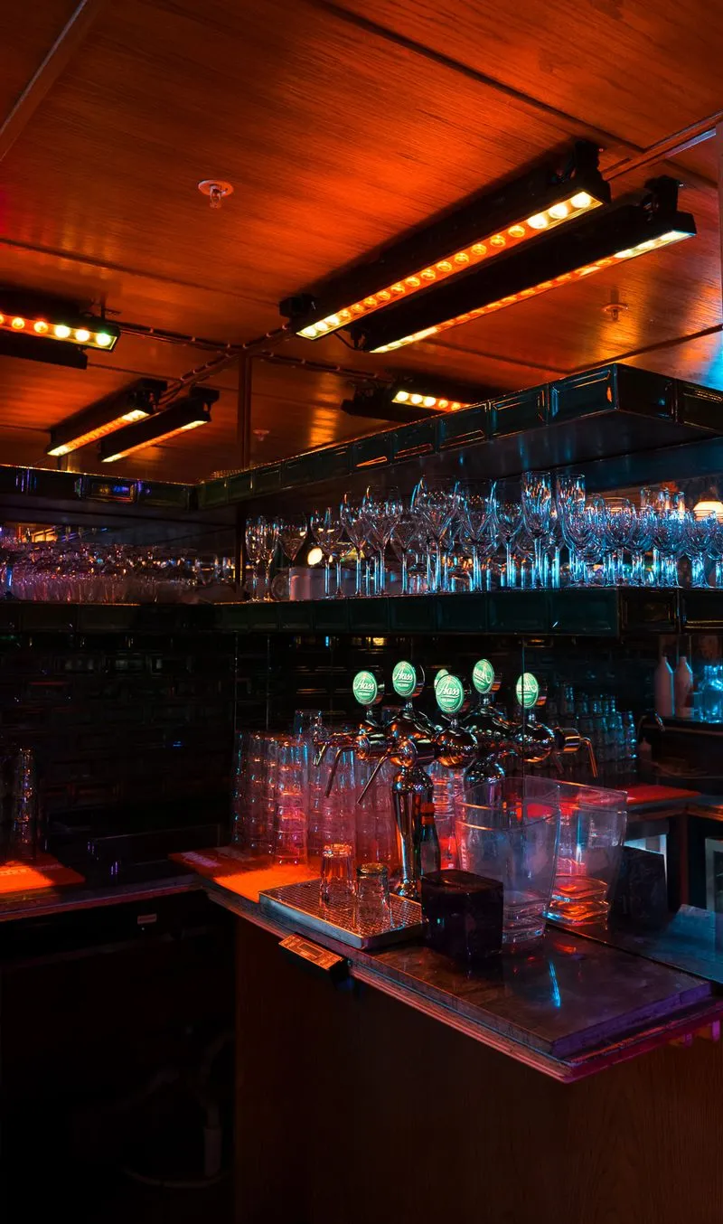 Detalj fra baren i selskapslokalet til Riviera Restaurant i Oslo med ølkraner, vinglass og stemningsfull belysning.
