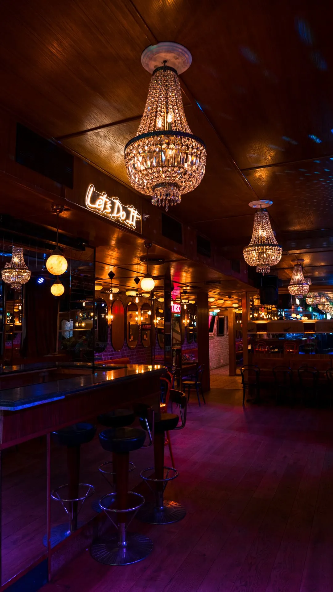 Stort selskapslokale hos Riviera Restaurant i Oslo med lysekroner, bardisk og neonskiltet Let's Do It i taket.
