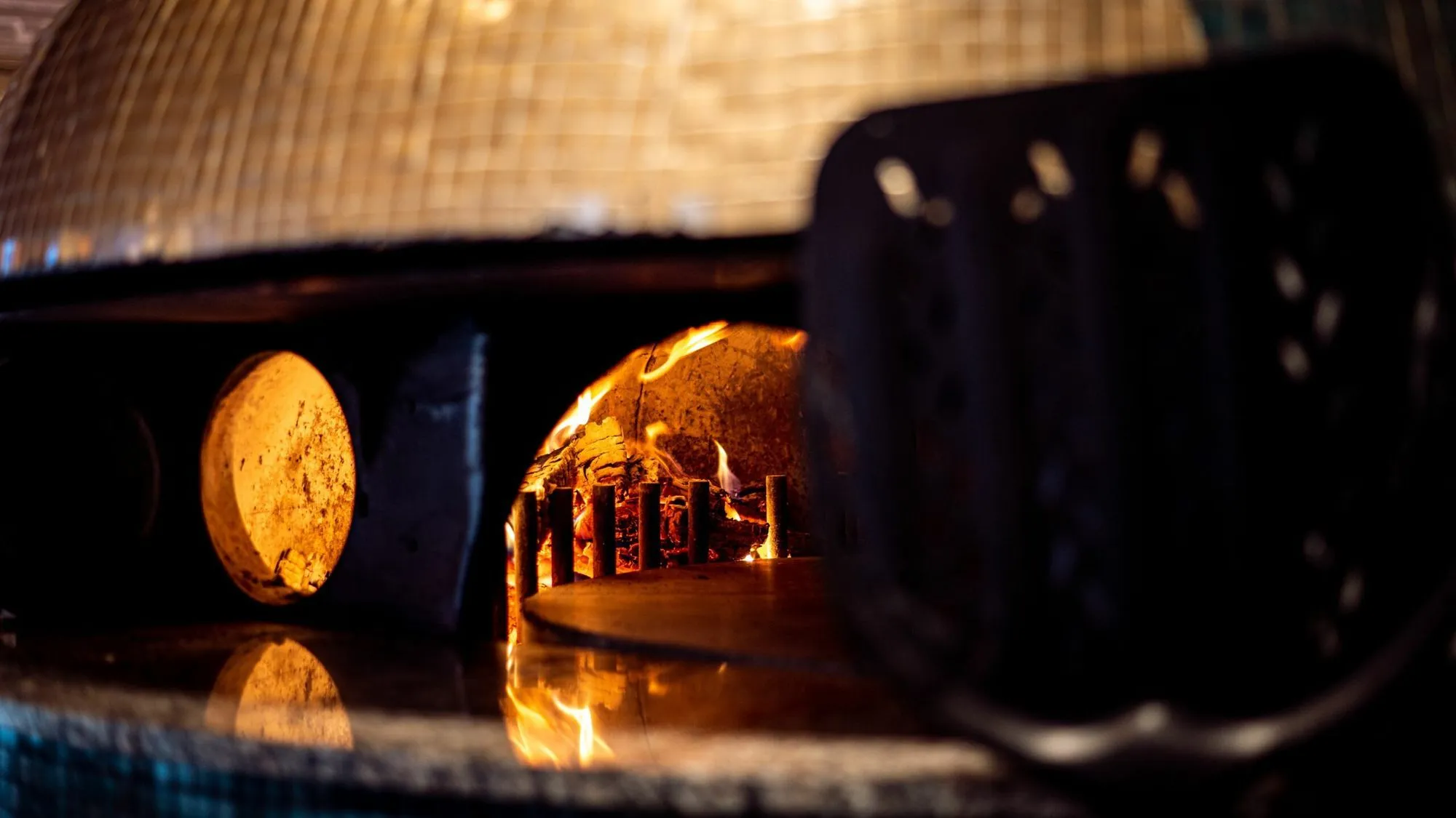 Vedfyrt pizzaovn hos Riviera Restaurant i Oslo med flammer og varme steinflater, brukt til autentisk italiensk pizzabaking.