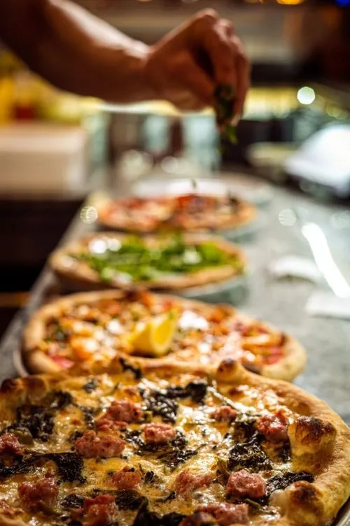 Håndlaget italiensk pizza toppes med ferske urter på Riviera Restaurant i Oslo, med flere varianter klare til servering.
