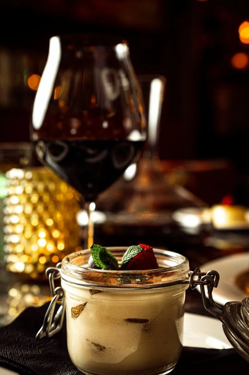 Italiensk tiramisu servert i glasskrukke på Riviera Restaurant i Oslo, med frisk jordbær, mynte og et glass rødvin i bakgrunnen.
