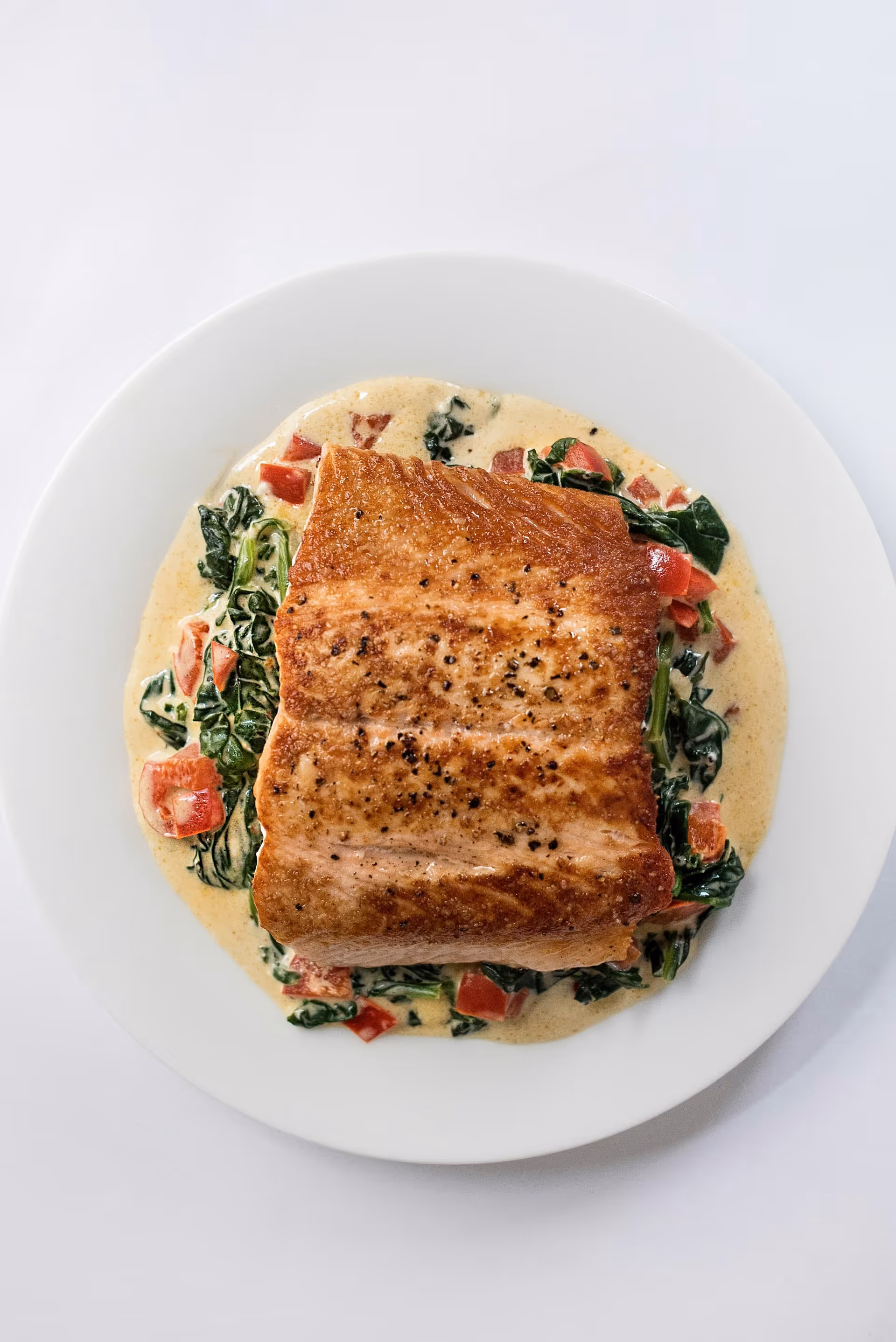 Perfekt stekt laksefilet servert med kremet saus, spinat og paprika – hovedrett hos Riviera Restaurant i Oslo