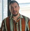 Mann mit gestreiftem Hemd steht vor einem Fenster und blickt freundlich in die Kamera