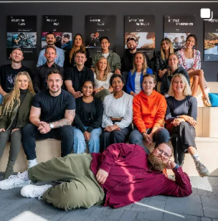 Gruppenfoto von etwa 20 Personen, die fröhlich auf Stufen posieren, mit einer Person liegend im Vordergrund