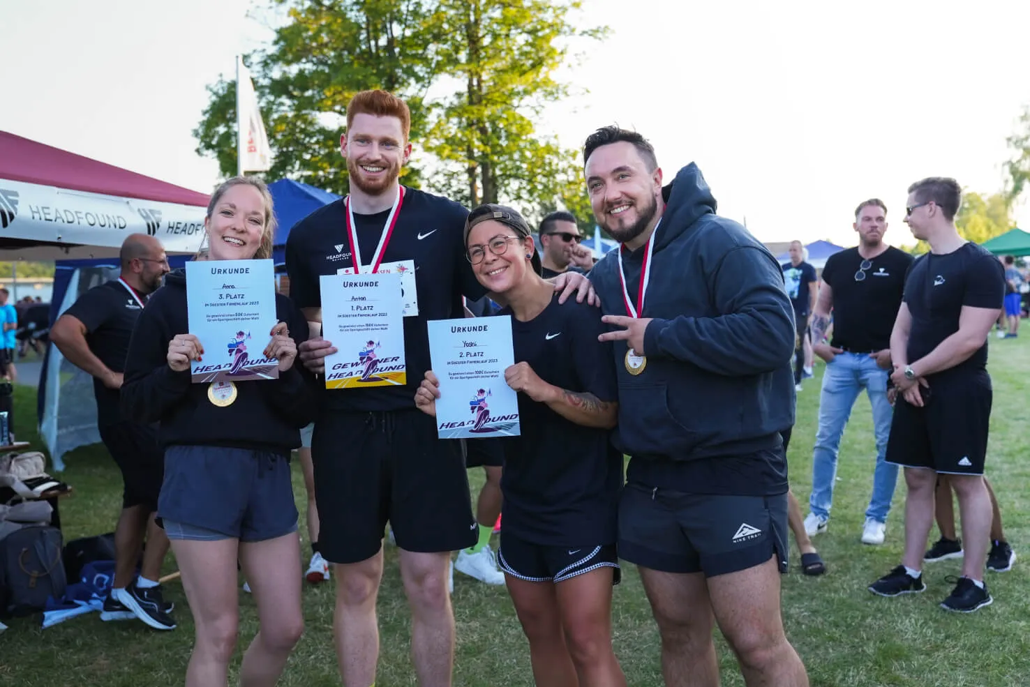 Vier Personen stehen lachend mit Urkunden und Medaillen im Freien nach einem sportlichen Event