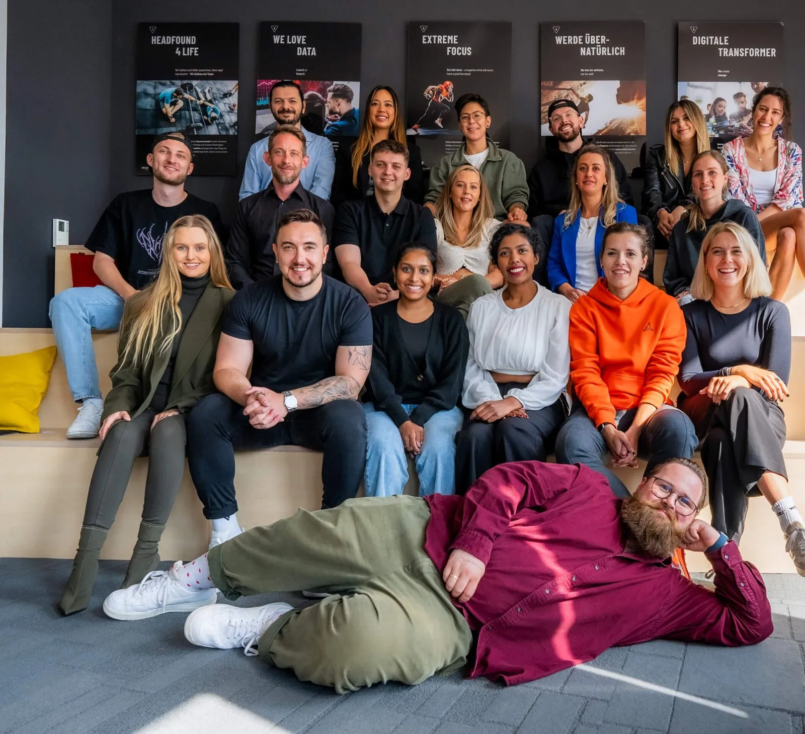 Eine größere Gruppe von Menschen posiert gemeinsam für ein Gruppenfoto in einem modernen, hellen Raum