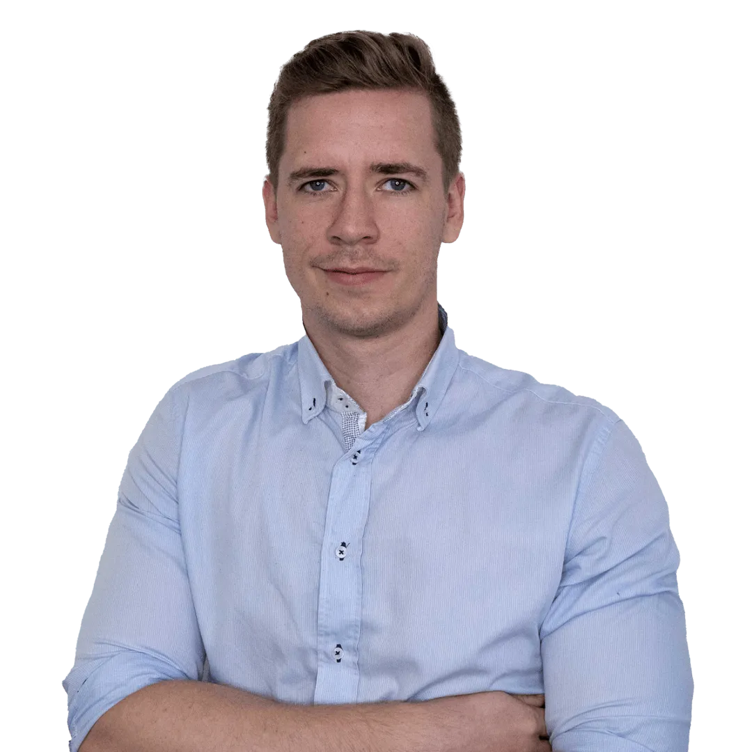 Mann mit hellem Hemd blickt in die Kamera und steht mit verschränkten Armen 