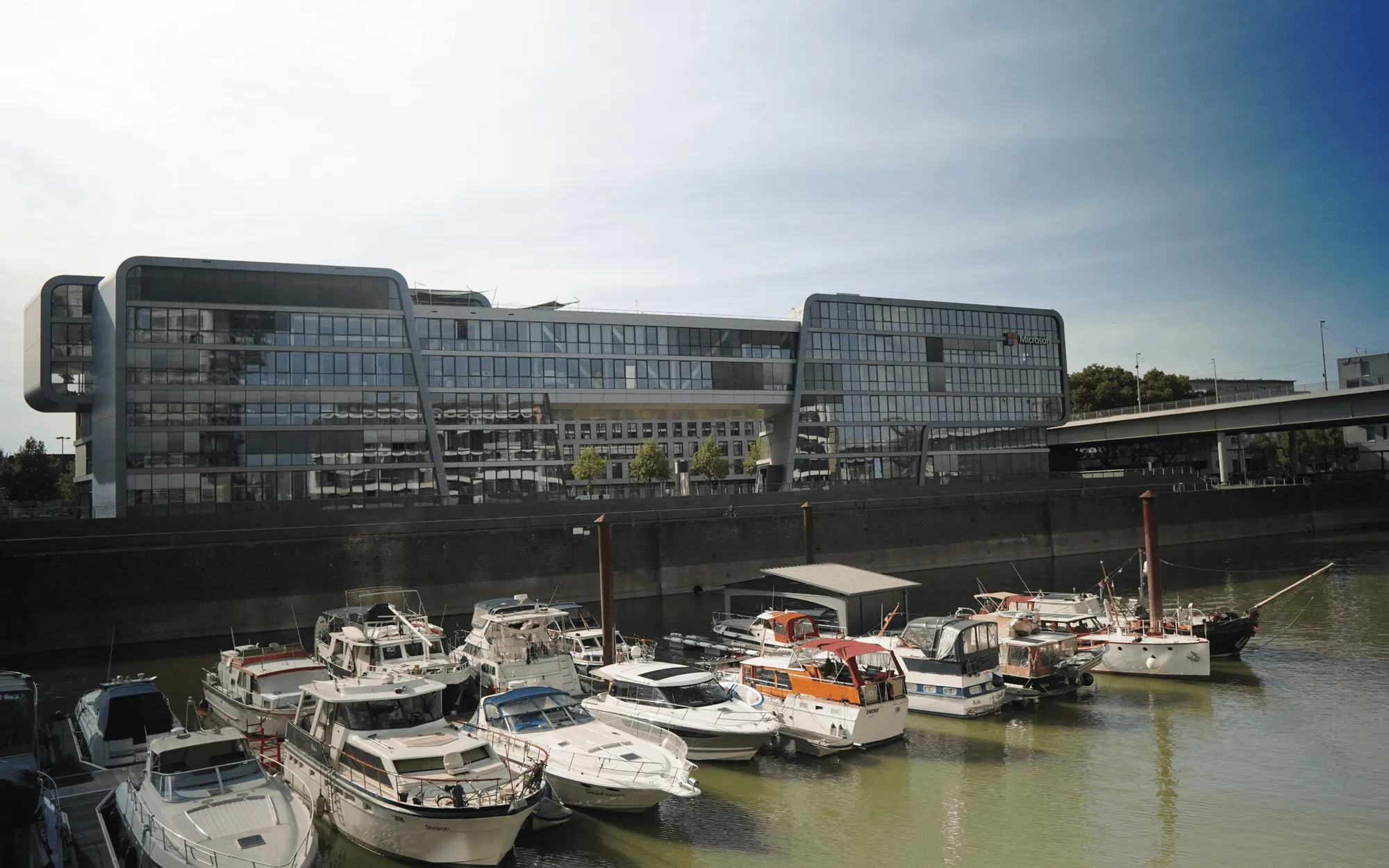Moderne Bürogebäude am Wasser mit vertäuten Booten im Vordergrund bei sonnigem Wetter