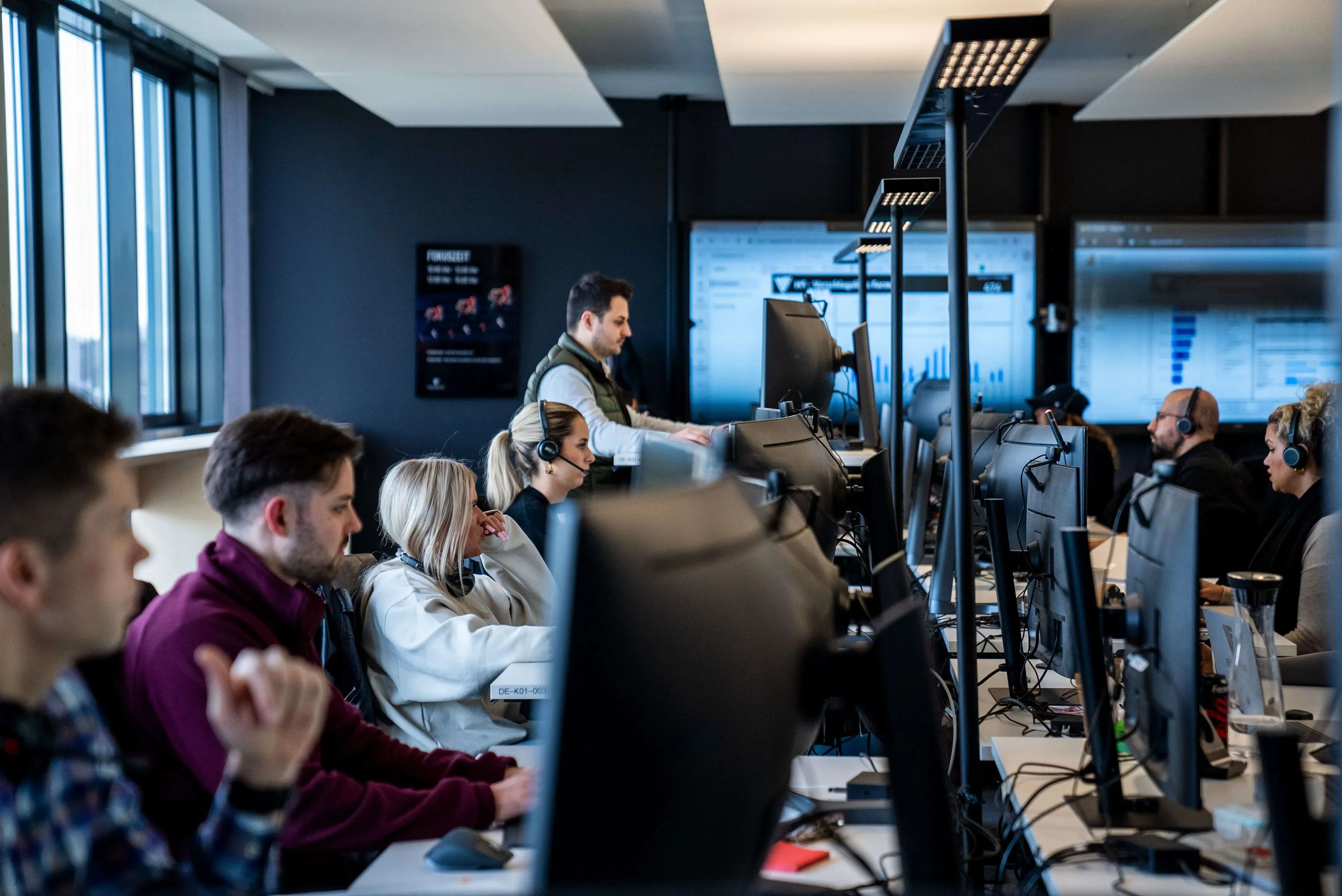 Mehrere Mitarbeitende mit Headsets arbeiten konzentriert an ihren Schreibtischen in einem modernen Großraumbüro