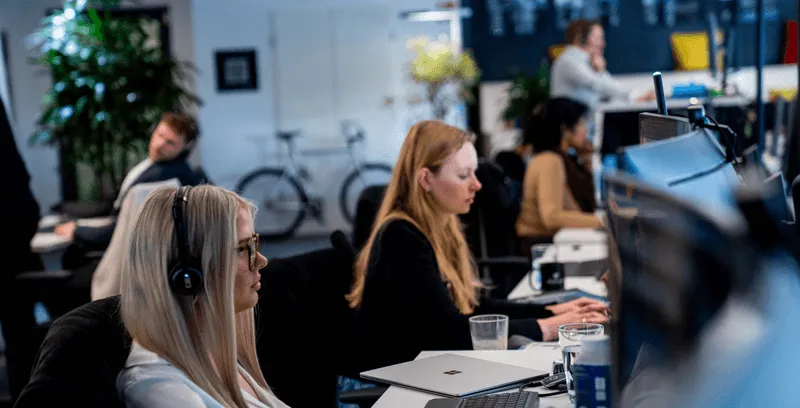 Mehrere Personen mit Headsets arbeiten an Schreibtischen in einem modernen Büro