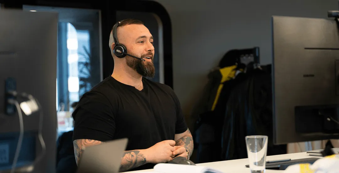 Mann mit Headset sitzt an einem Schreibtisch vor zwei Monitoren