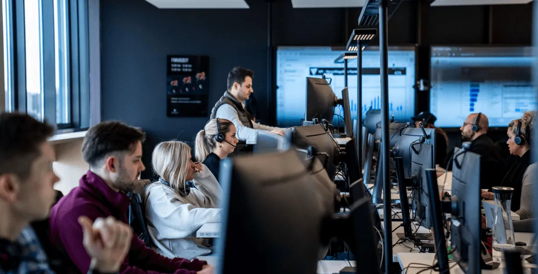 Mehrere Personen arbeiten konzentriert an ihren Computern in einem modernen Büro mit vielen Monitoren