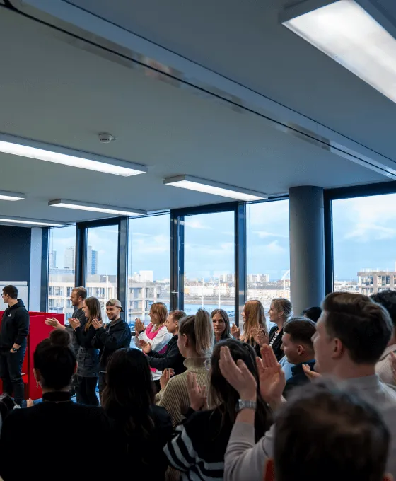 Eine Gruppe von Menschen sitzt in einem Raum mit großen Fenstern und applaudiert