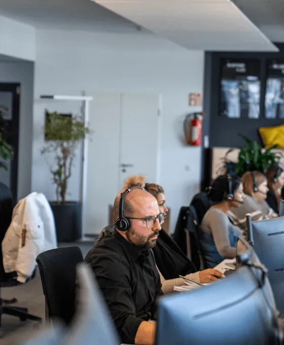 Mann mit Headset sitzt an einem Schreibtisch vor einem Monitor in einem Büro