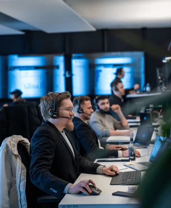 Mehrere Personen arbeiten konzentriert an ihren Computern in einem modernen Büro mit Headsets und großen Bildschirmen