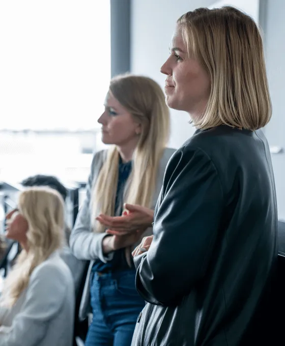 Drei Frauen hören aufmerksam zu, stehen und sitzen nebeneinander in einem modernen, hellen Büro 