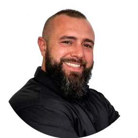 Lächelnder Mann mit Bart und schwarzem Hemd vor weißem Hintergrund, verschränkte Arme, Blick in die Kamera