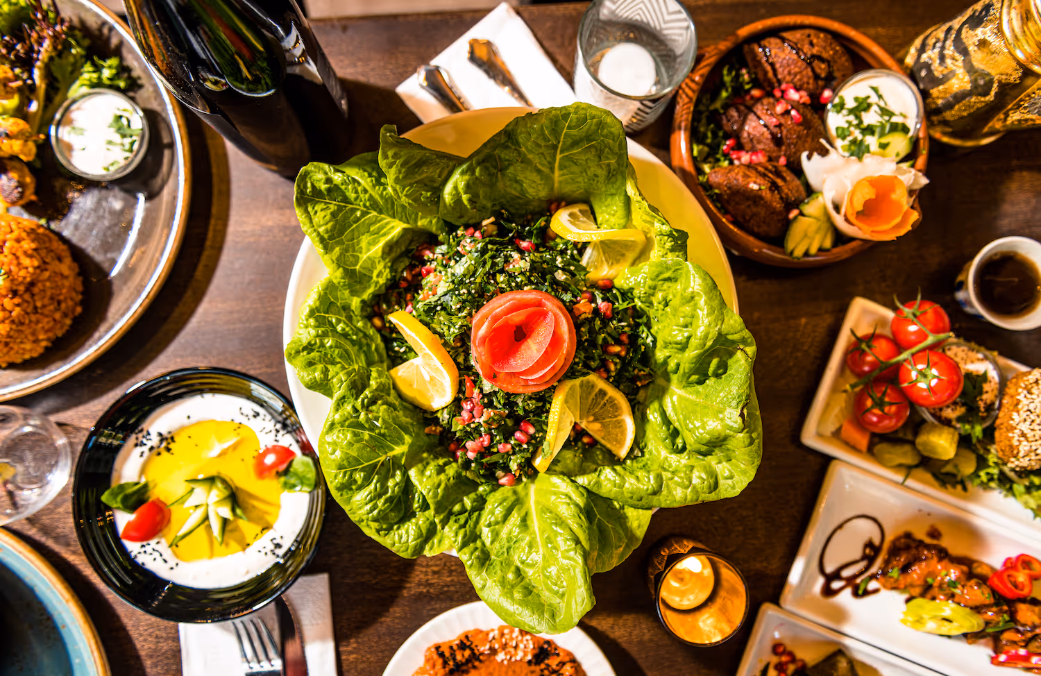Et fargerikt utvalg av meze-retter fra Midtøsten, med tabbouleh servert i salatblader, hummus, falafel og grillede grønnsaker på et rustikt trebord hos KosKos Restaurant.
