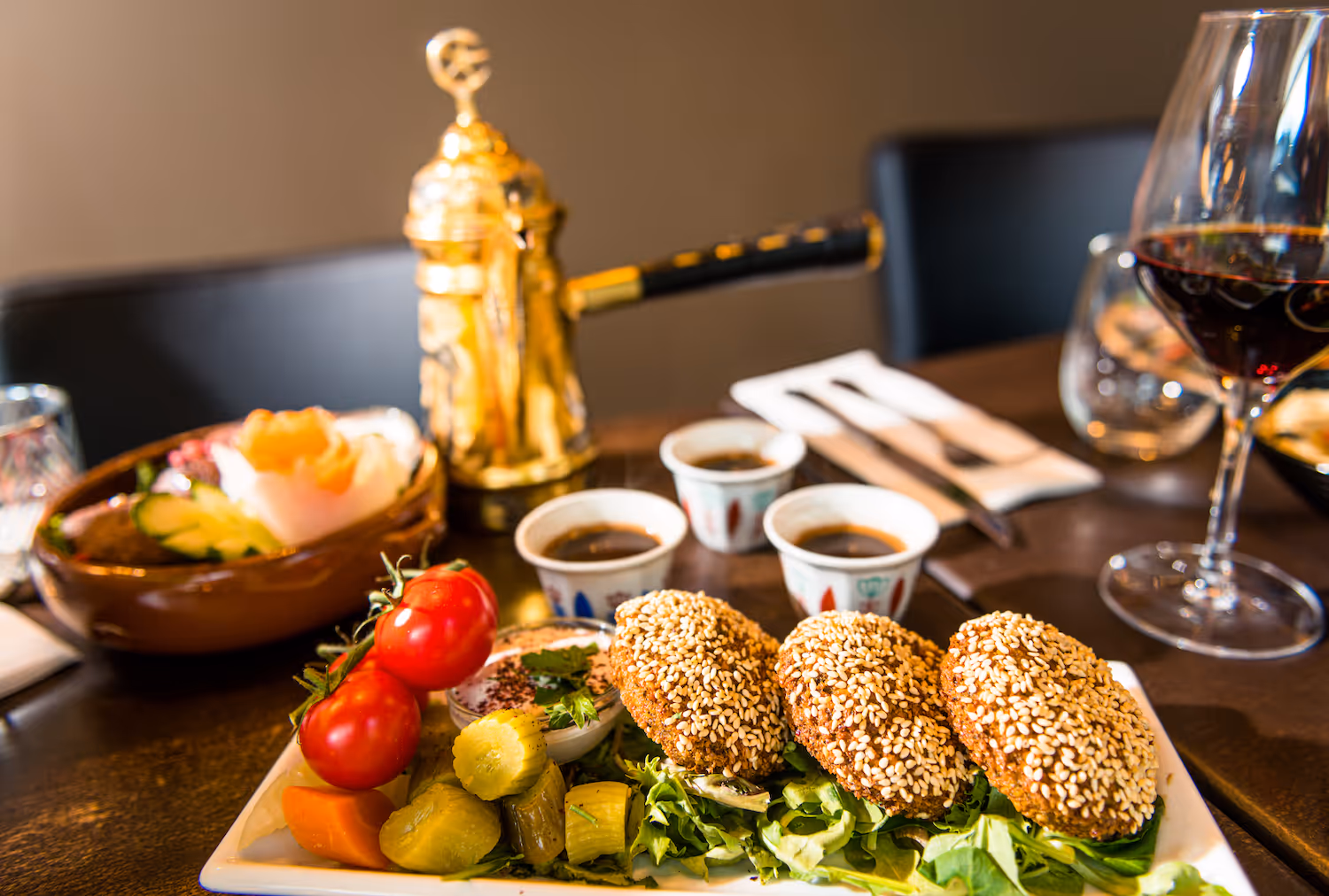 Sprø falafel dekket med sesamfrø servert med friske grønnsaker, syltet tilbehør og dip – akkompagnert av arabisk kaffe i tradisjonelle kopper og kaffekanne hos KosKos Restaurant.