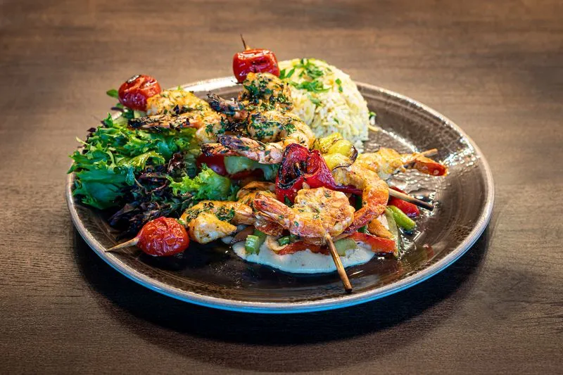 Grillspyd med scampi og grillede grønnsaker servert med kremet hummus, urteris og frisk salat – en delikat sjømatrett fra KosKos Restaurant.
