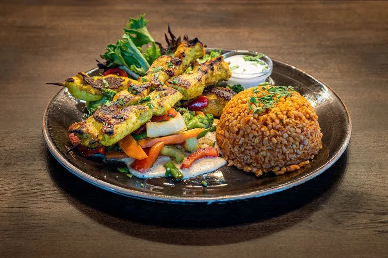 Grillspyd med saftig kjøtt og grønnsaker servert med bulgur, kremet saus og frisk salat – en klassisk hovedrett fra KosKos Restaurant.