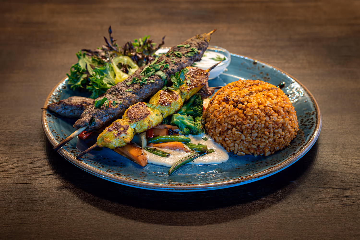 Grilltallerken fra KosKos med saftig kebabspyd, kyllingspyd, bulgur, grillede grønnsaker, kremet saus og frisk salat – en ekte smak av Midtøsten.