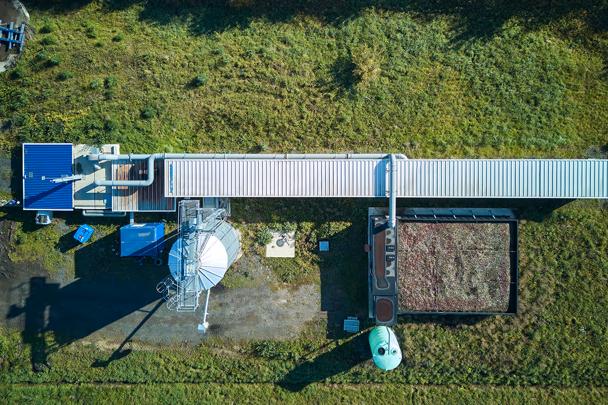 Luftaufnahme einer landwirtschaftlichen Anlage mit Silos, Rohren und einem bepflanzten Dach auf grünem Grasland.
