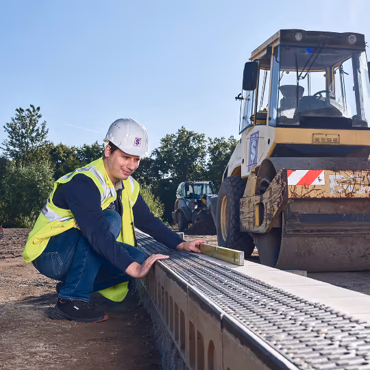 Bauarbeiter mit Helm und Warnweste überprüft die Ausrichtung einer Betonmauer mit Wasserwaage auf einer Baustelle.