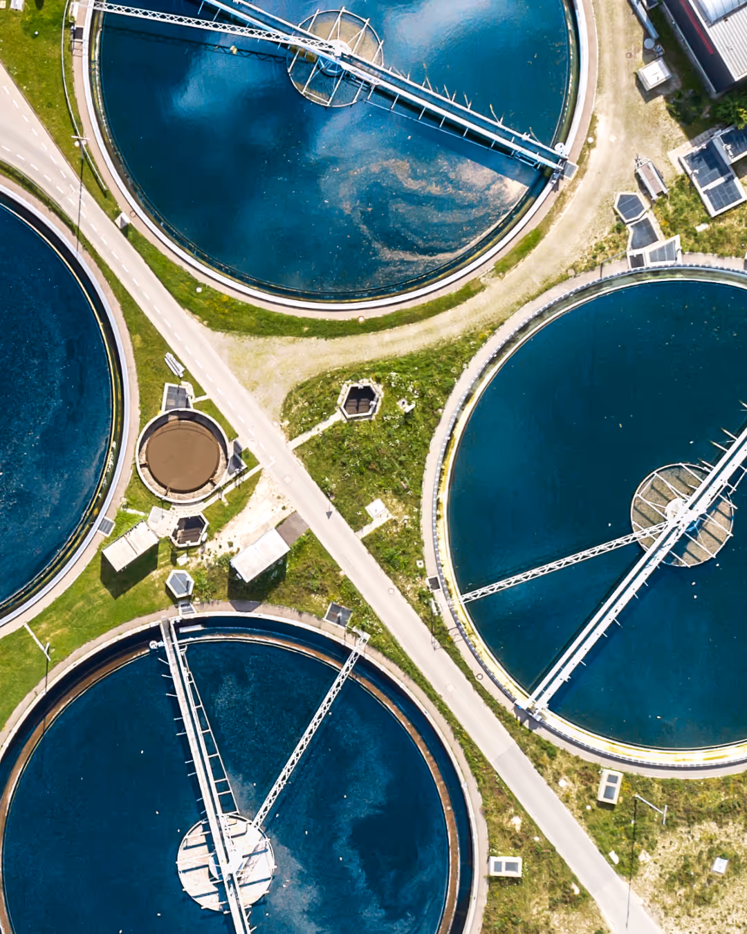 Luftaufnahme eines Klärwerks mit mehreren runden Absetzbecken und angrenzenden Wegen und Gebäuden.