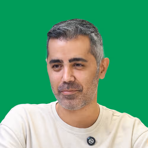 Middle-aged man with short gray and black hair wearing a light beige shirt against a green background.