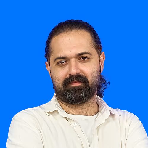 Man with dark hair and beard wearing a white shirt against a blue background.