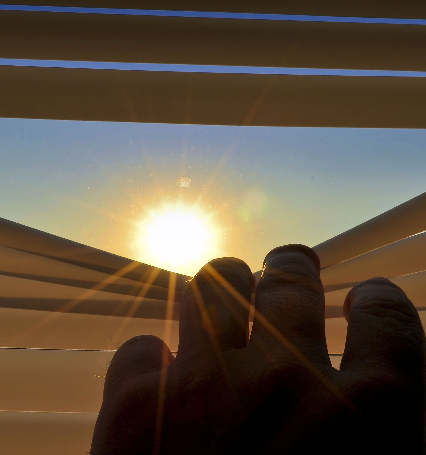 Person peeking through blinds at the sun