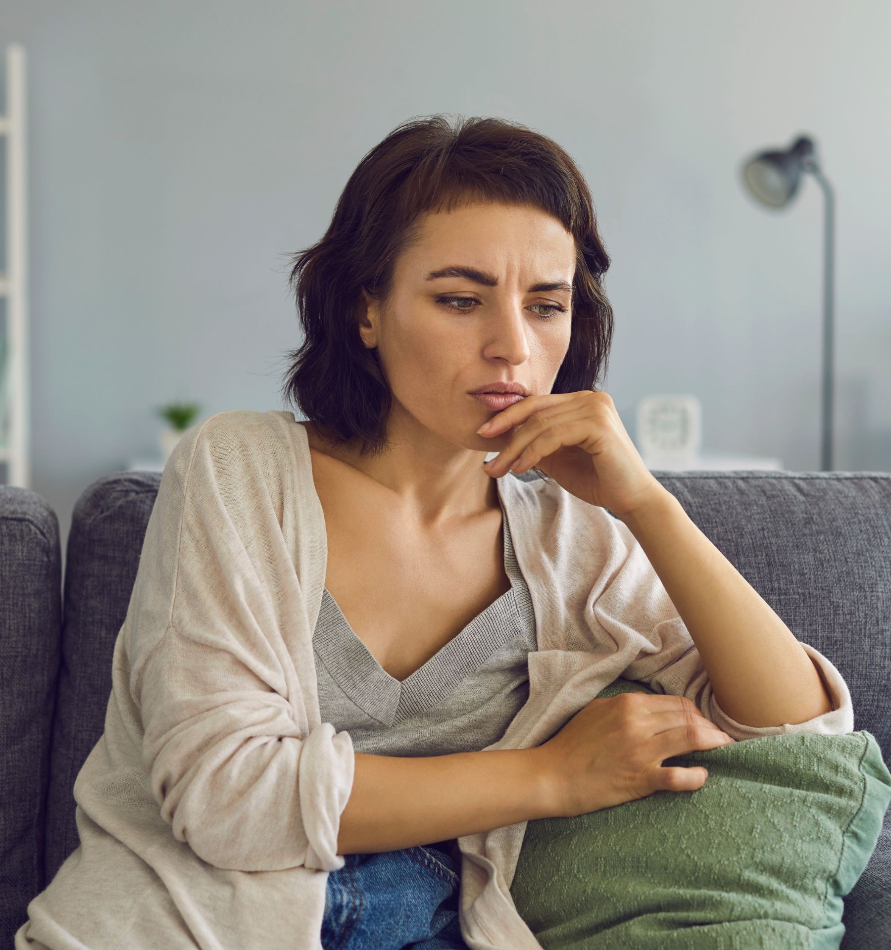 A woman sits on a couch looking thoughtful
