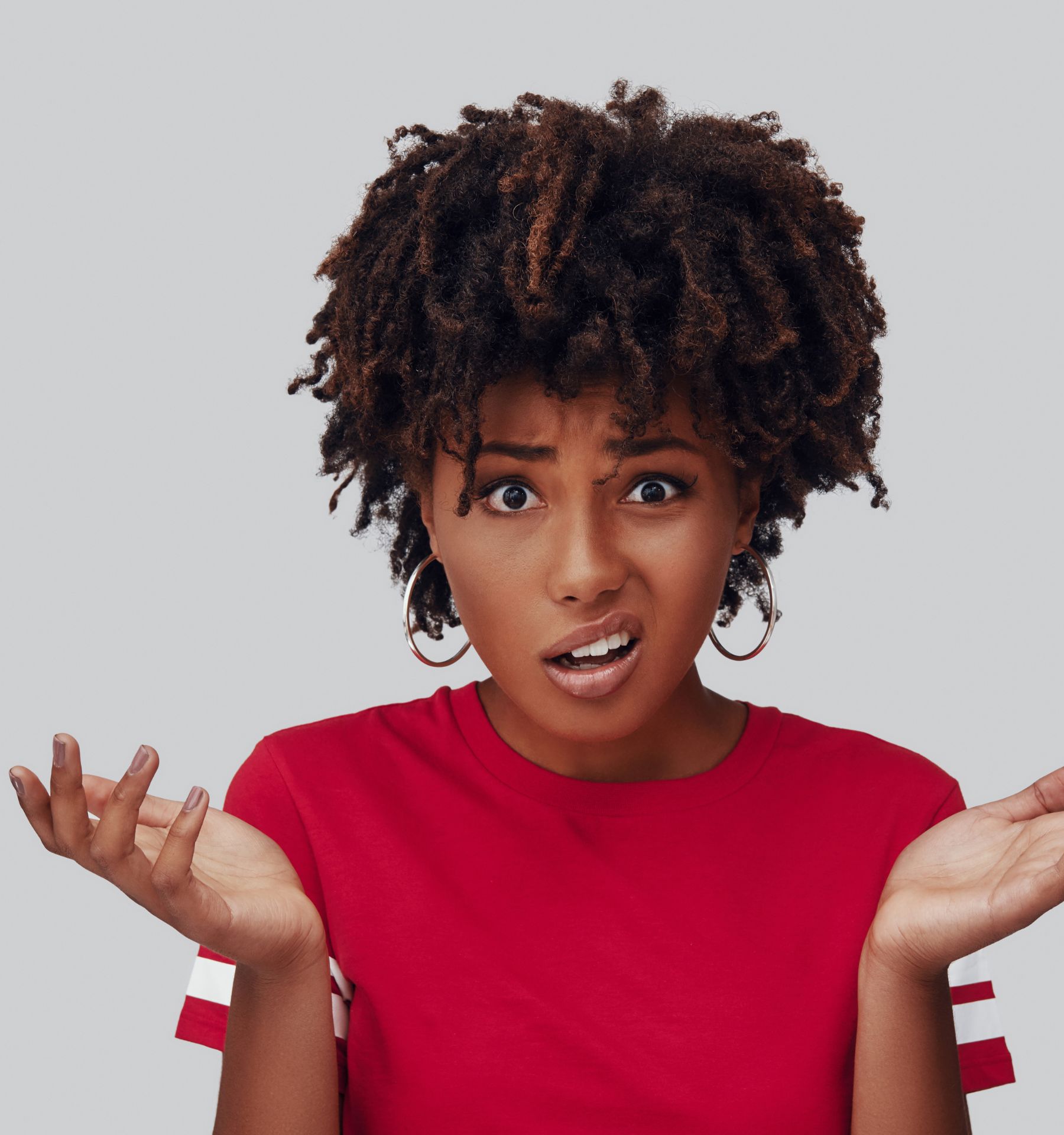 A person with tight curly brown hair, wearing a red top looks frustrated