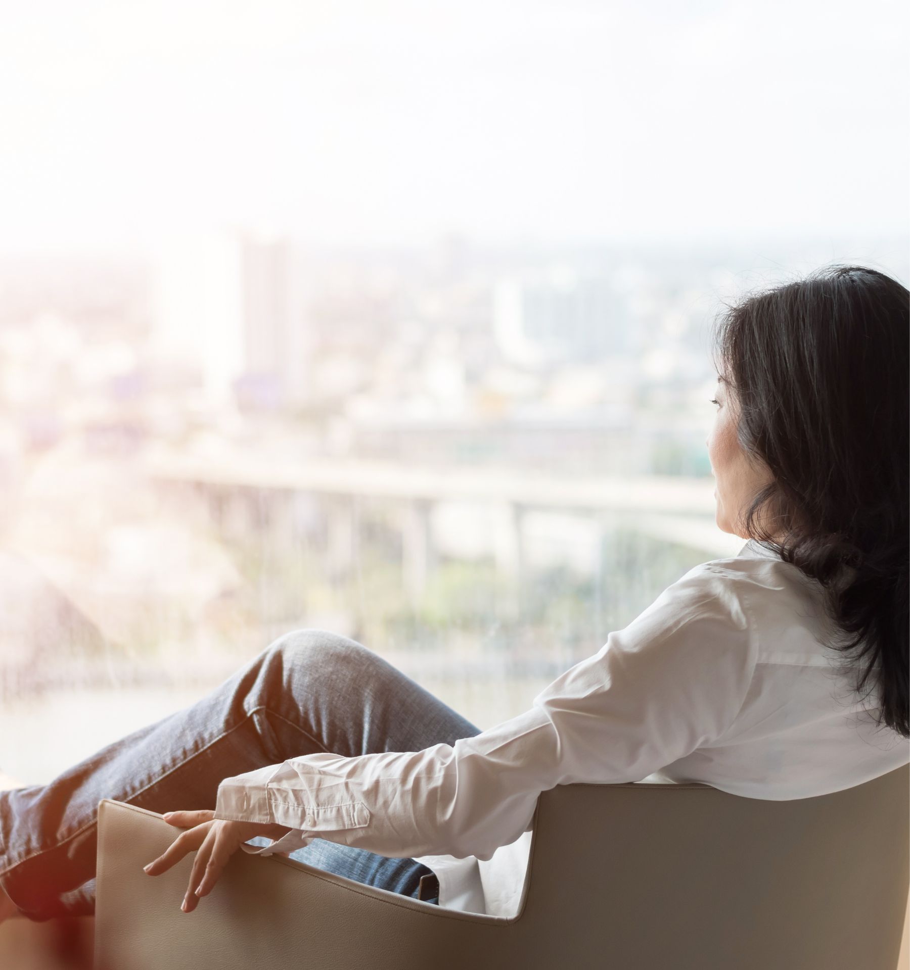 Woman with long dark hair, white shirt and jeans sitting and looking out of window