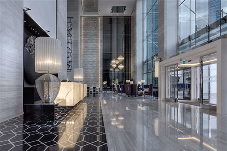 Luxurious hotel lobby with polished marble floors, modern interior design, elegant lighting, and high glass windows creating a bright upscale atmosphere.