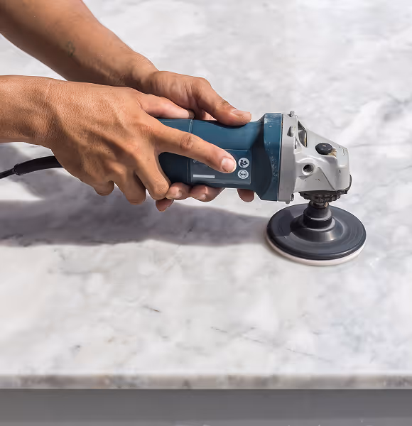 Close-up of worker polishing marble surface with handheld machine for professional stone restoration and shine enhancement.